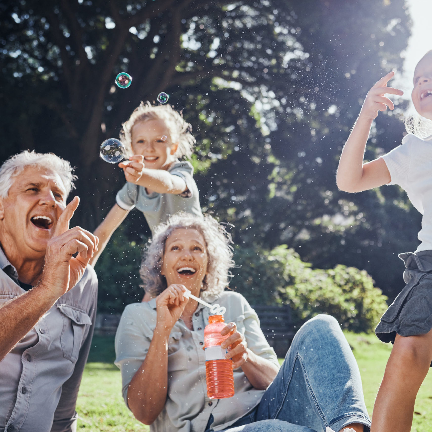 Grandparents, bubbles and children play in park happy together for fun, joy and outdoor happiness. Retired, smile and excited elderly senior couple, girl grandkids and love playing outside in nature.